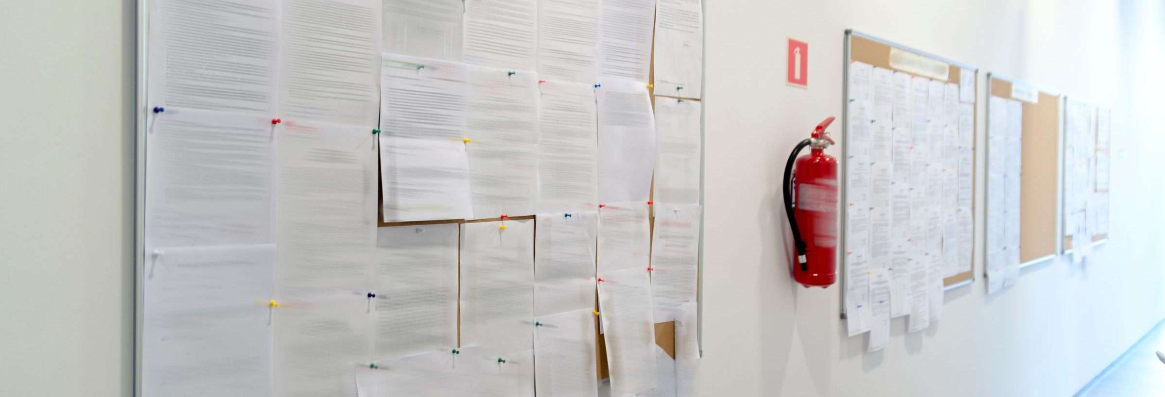 Das Bild zeigt ein schwarzes Brett mit Aushängen auf einem Flur.